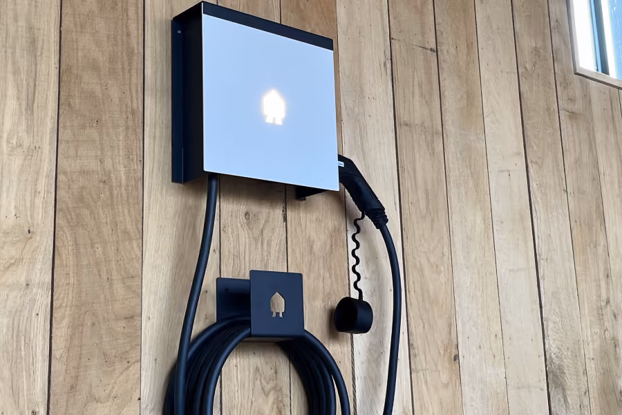 Wandgemonteerde elektrische laadstation met kabel op houten achtergrond.