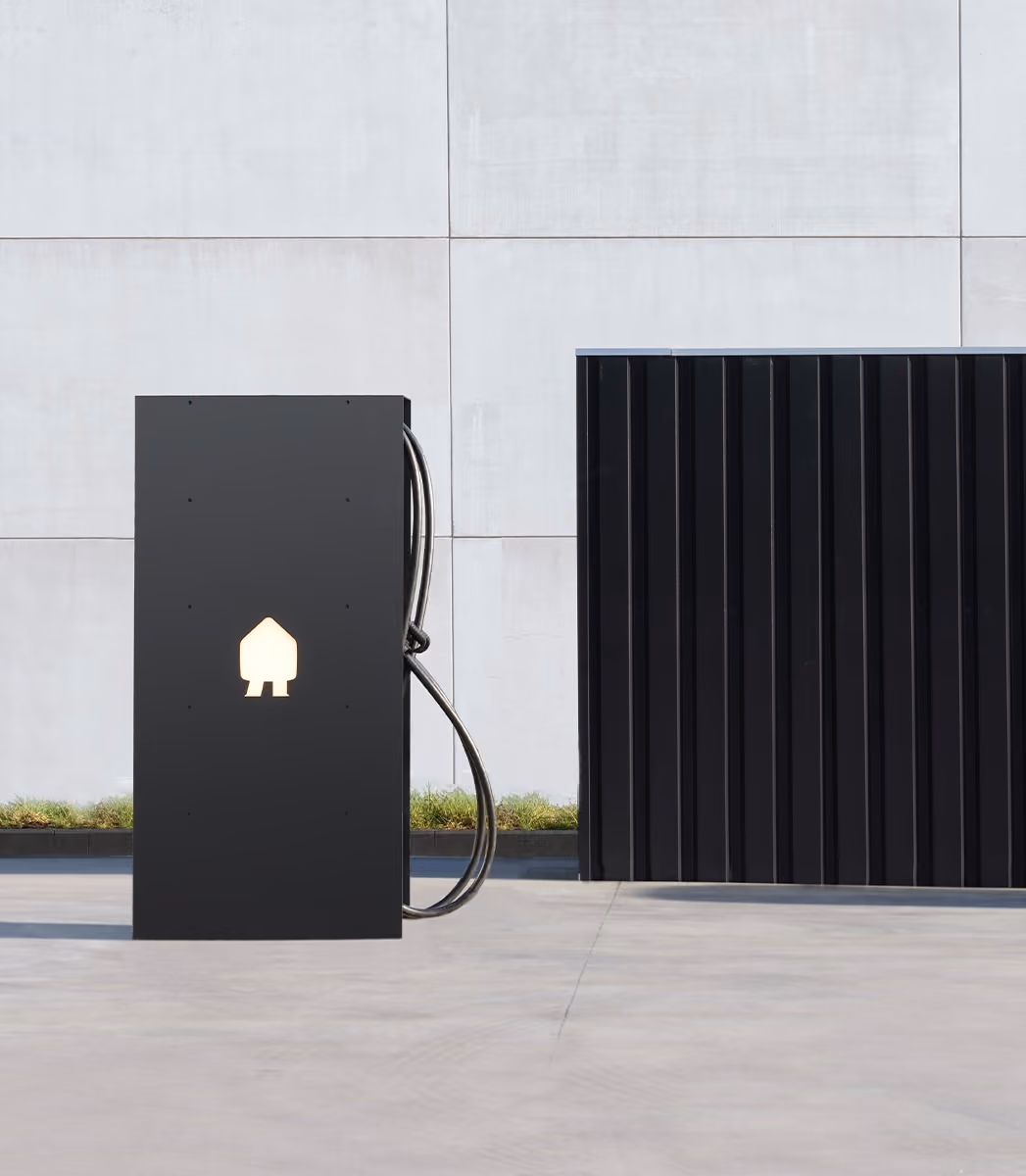 Zwarte elektrische laadpaal met lichtgevend Smappee logo, geplaatst op een betonnen vloer voor een lichte betonnen muur.