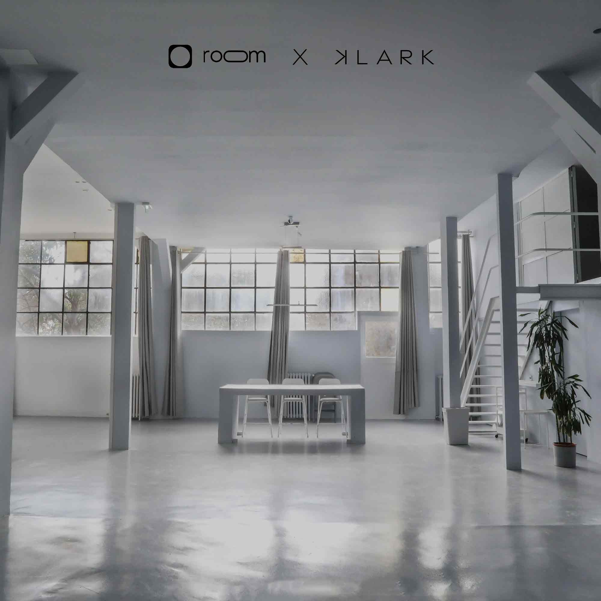 Intérieur spacieux et minimaliste avec table blanche, trois chaises, grandes fenêtres et escalier blanc menant à une mezzanine.