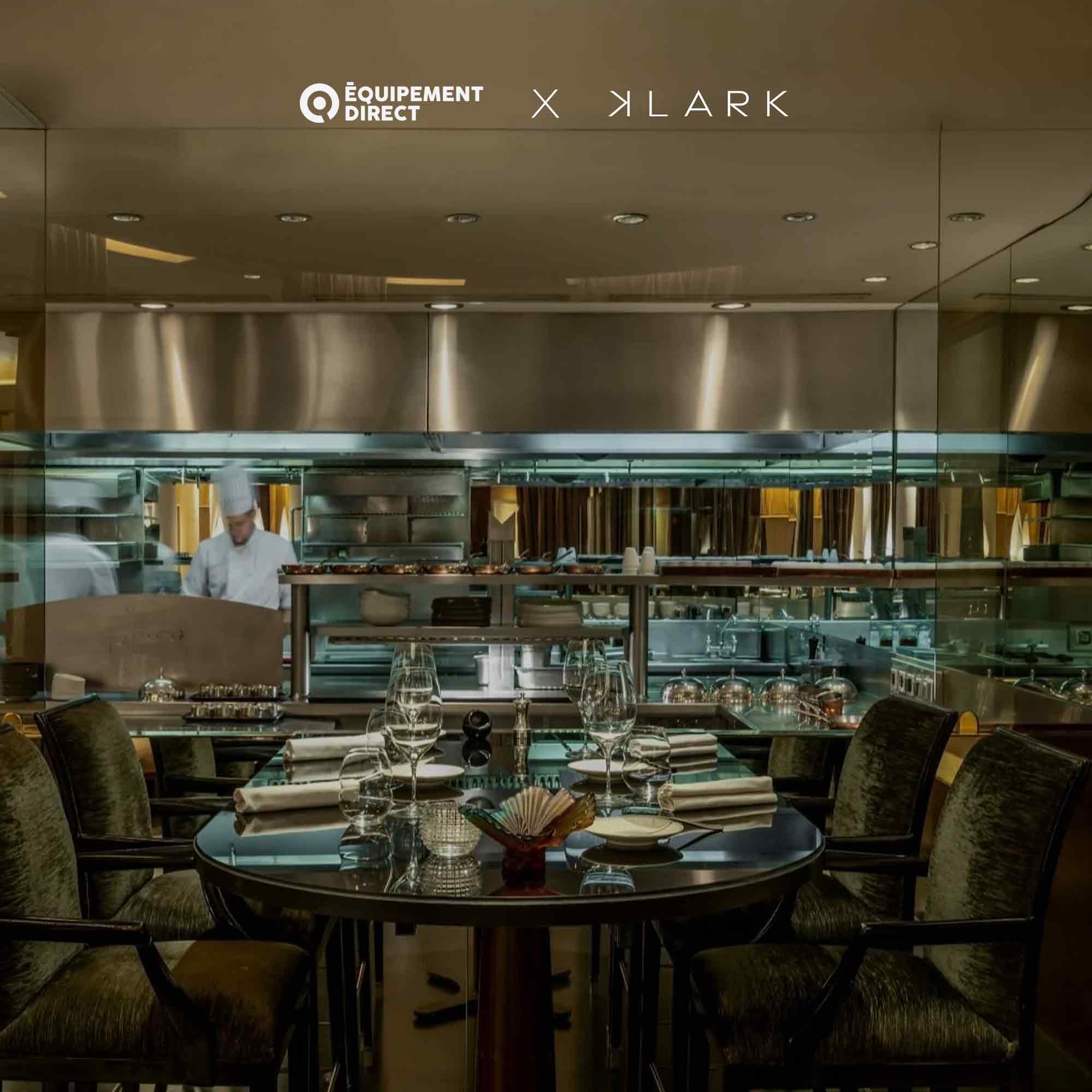 Table élégamment dressée pour quatre personnes dans un restaurant avec un chef cuisinier travaillant en cuisine ouverte en arrière-plan.