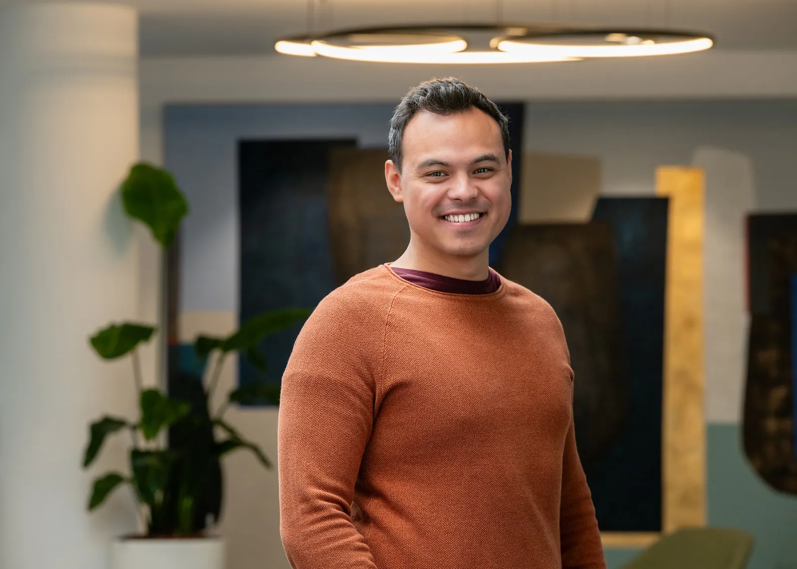 Kevin Struik souriant portant un pull marron foncé dans un bureau moderne avec des plantes en arrière-plan.