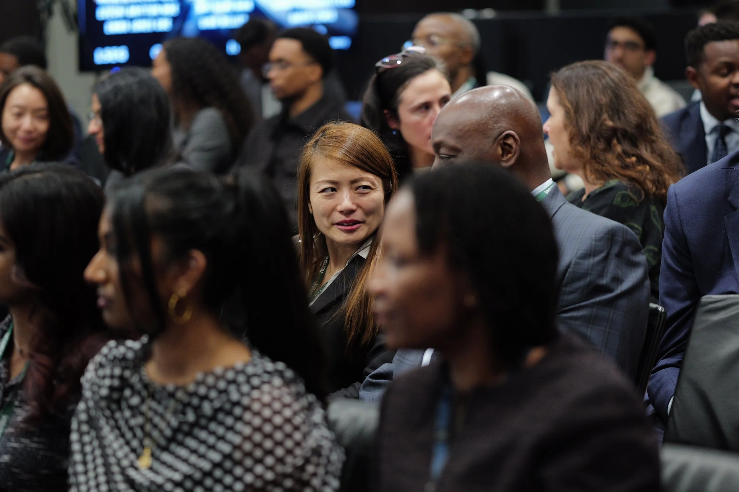 Diverse group of people seated indoors, some engaged in conversation.