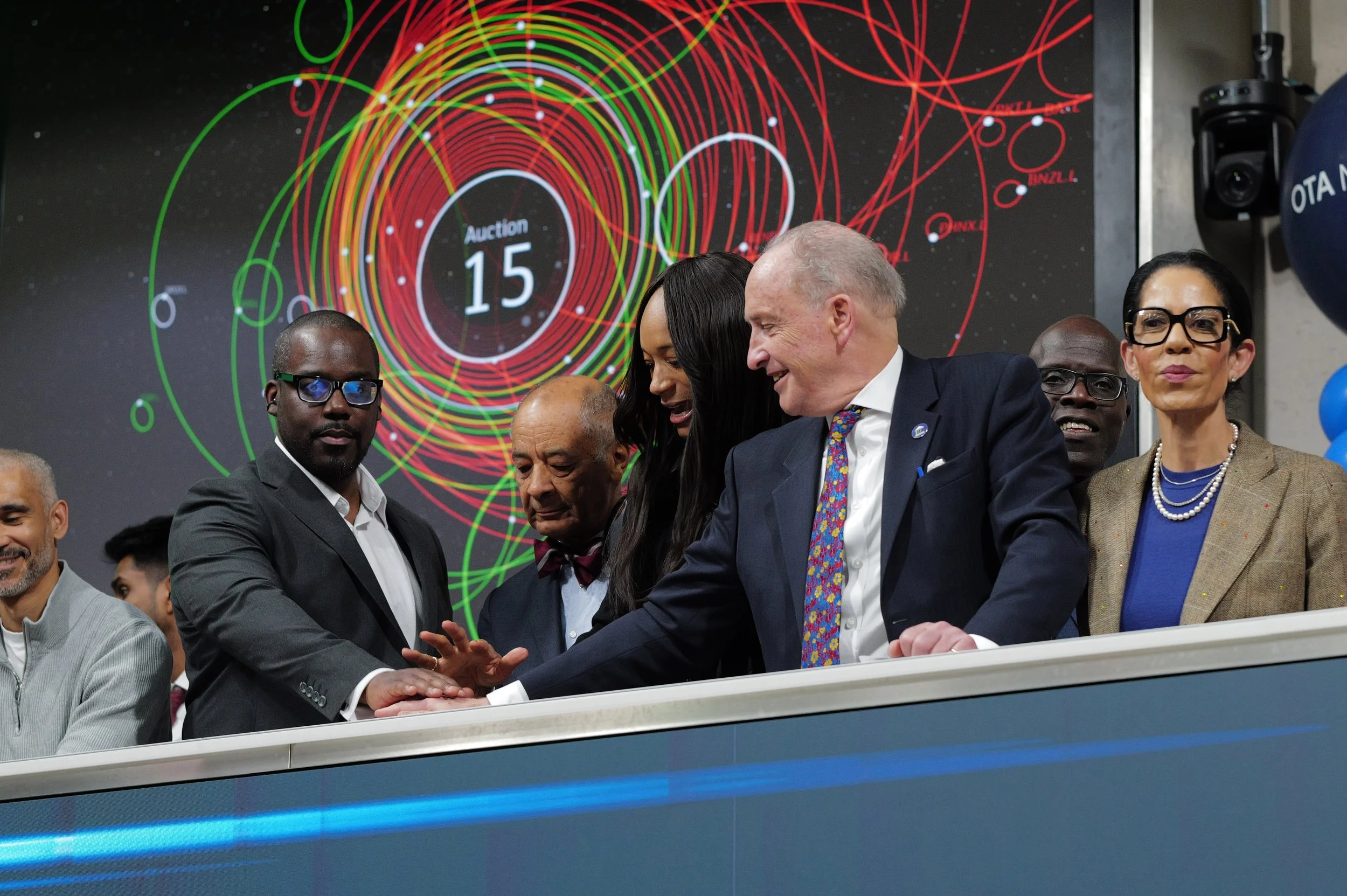 Group of diverse professionals pressing a button together during a auction event with colorful circular graphics on screen behind them.