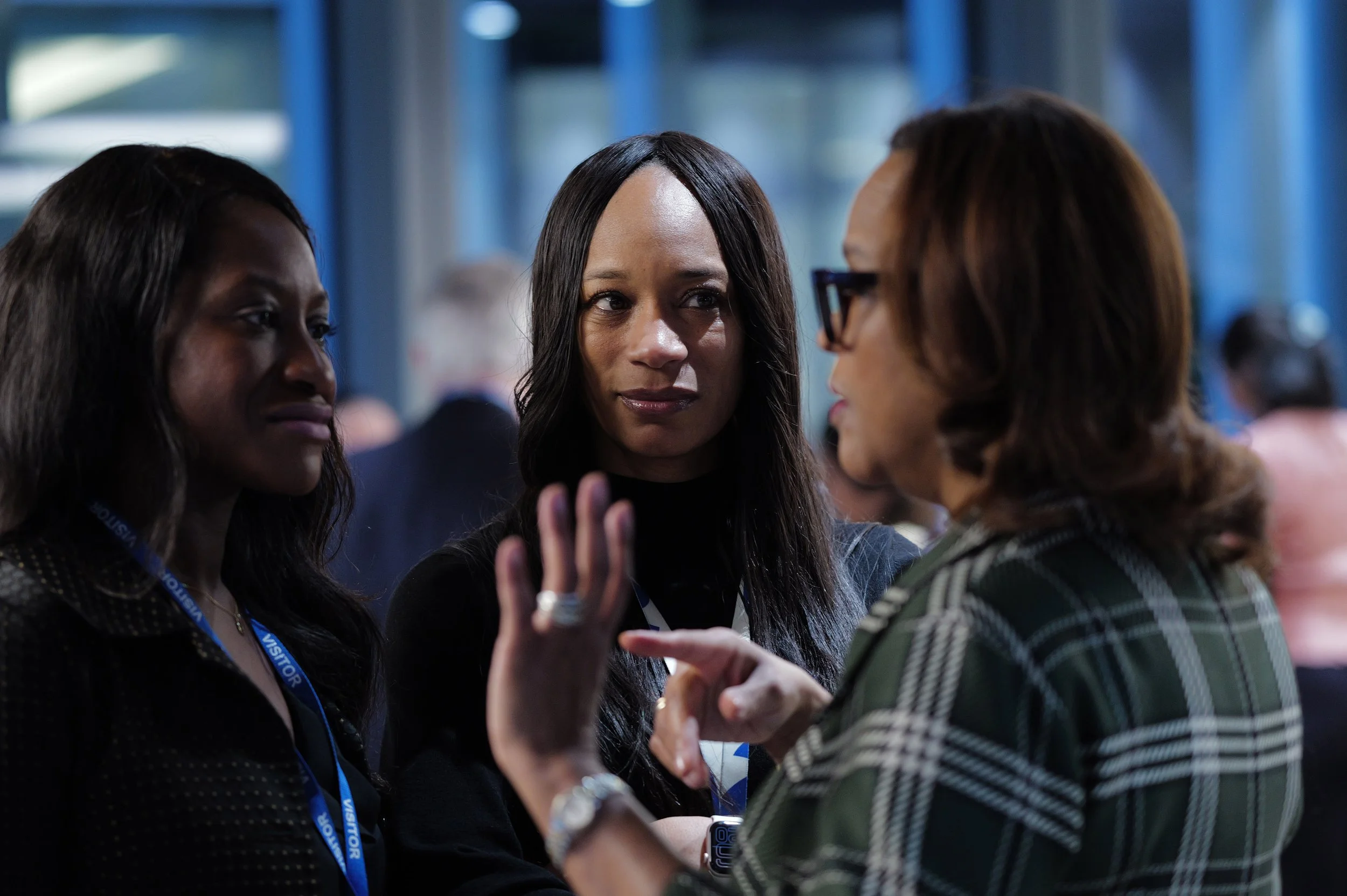 Three professional women engaged in a serious conversation in an office setting.
