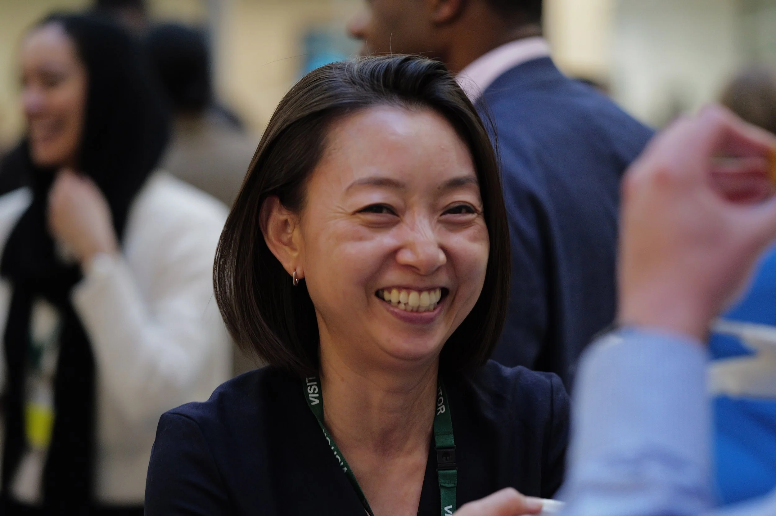 Smiling woman with short dark hair wearing a dark top and a visitor badge at a social event.