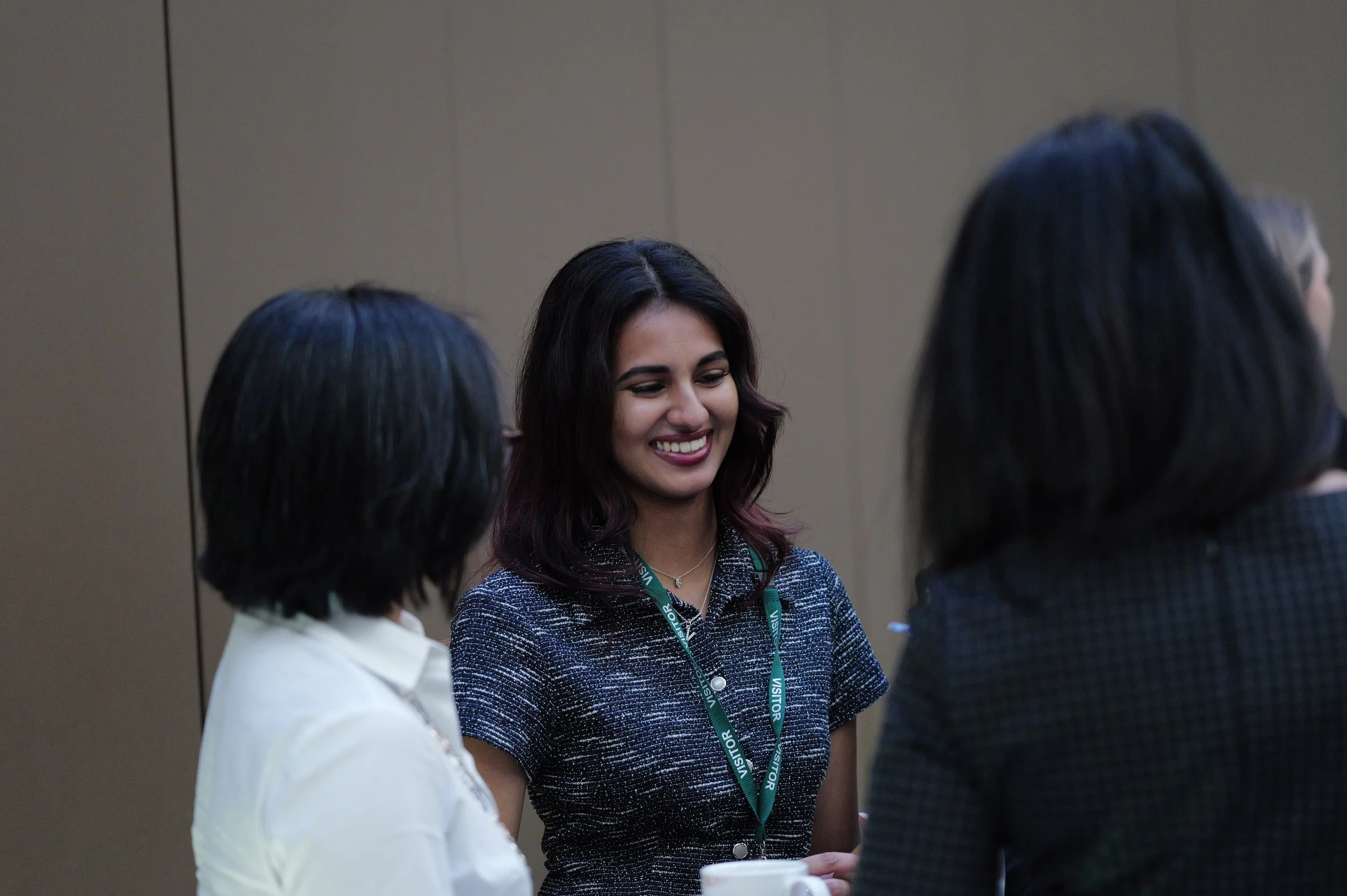 Smiling woman wearing a visitor badge talking with two other women in an indoor setting.