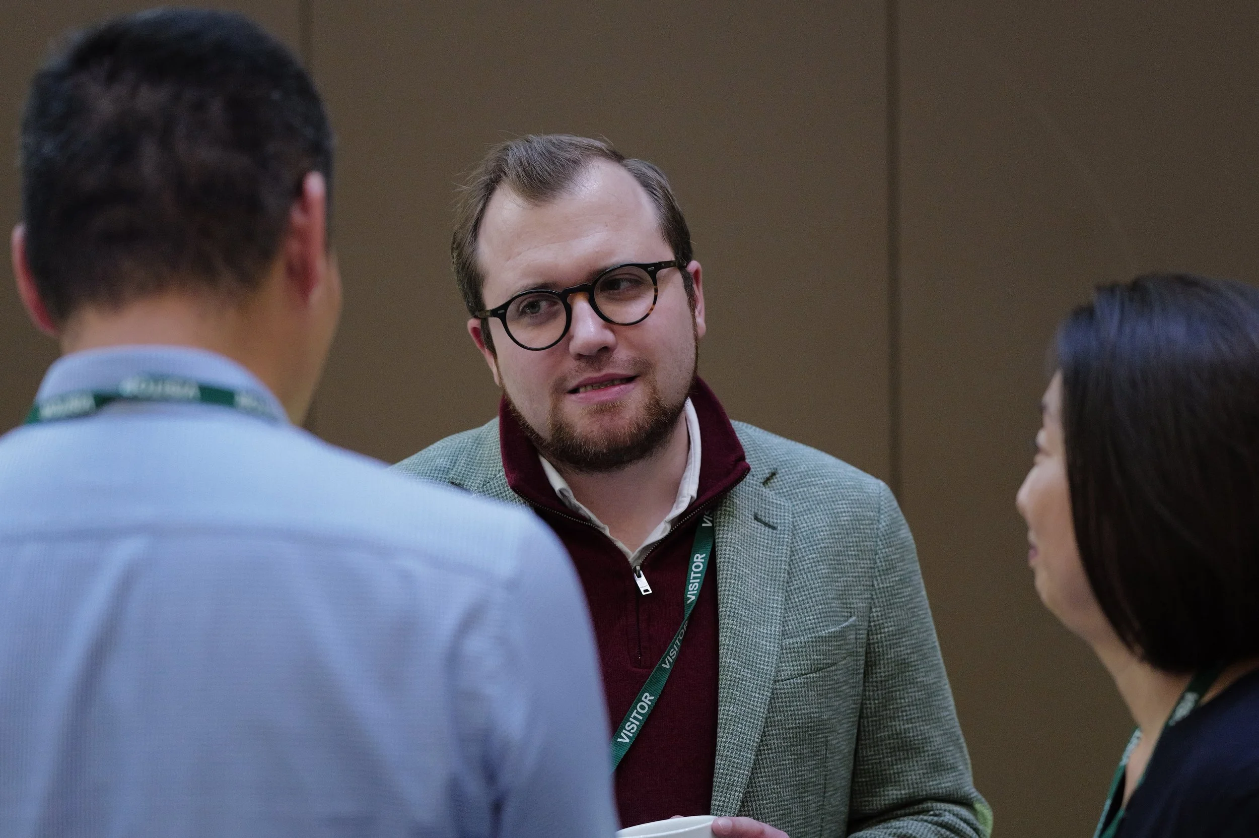 Three people engaged in conversation, a man with glasses in a checkered blazer facing two others.