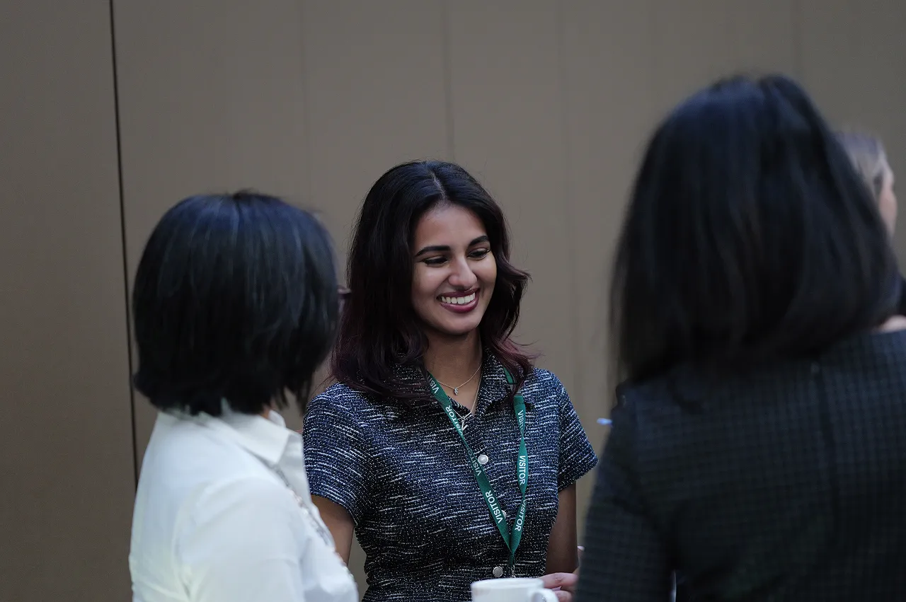 Young woman smiling and wearing a visitor lanyard while talking with two other women.