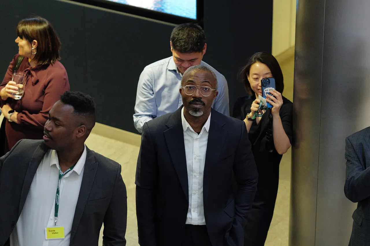 Group of diverse professionals at an event, including a man in glasses and suit looking at the camera.
