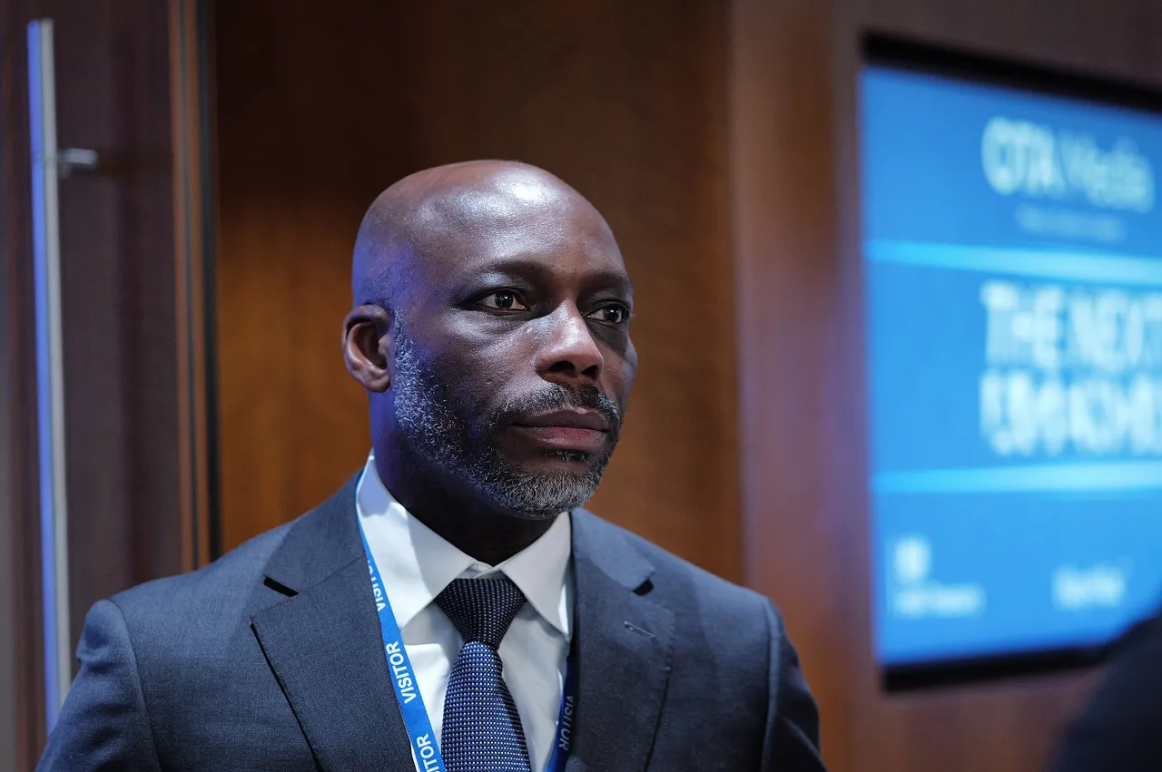 Man in a suit and tie with a visitor badge looking thoughtfully to the side in an indoor setting.