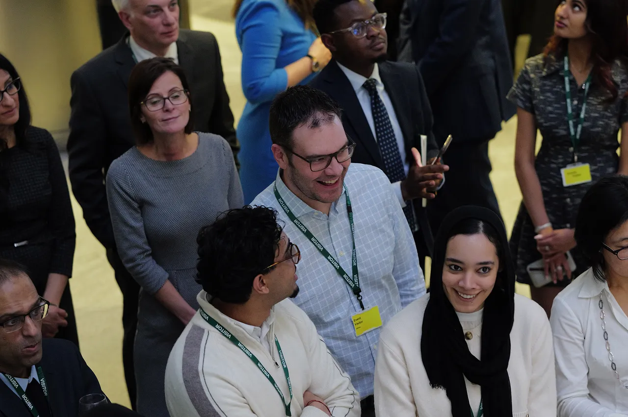 Group of professional-looking people wearing visitor badges engaged in conversation at an indoor event.