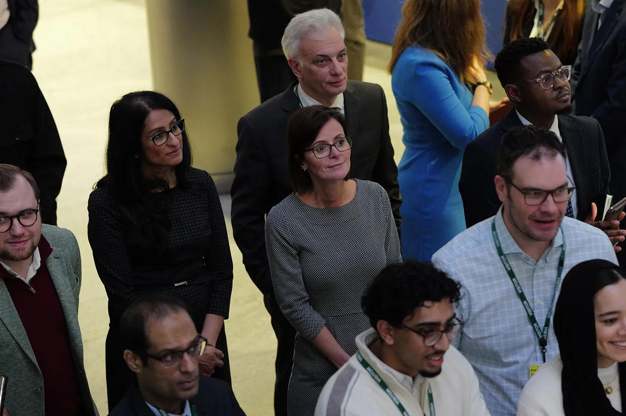 Group of diverse professionals wearing glasses and business attire standing and looking upwards attentively.