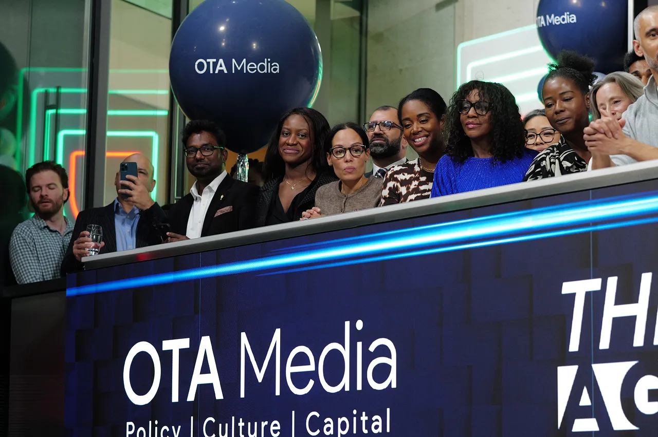 Group of diverse people standing behind a digital board displaying 'OTA Media Policy | Culture | Capital' with OTA Media balloons in the background.