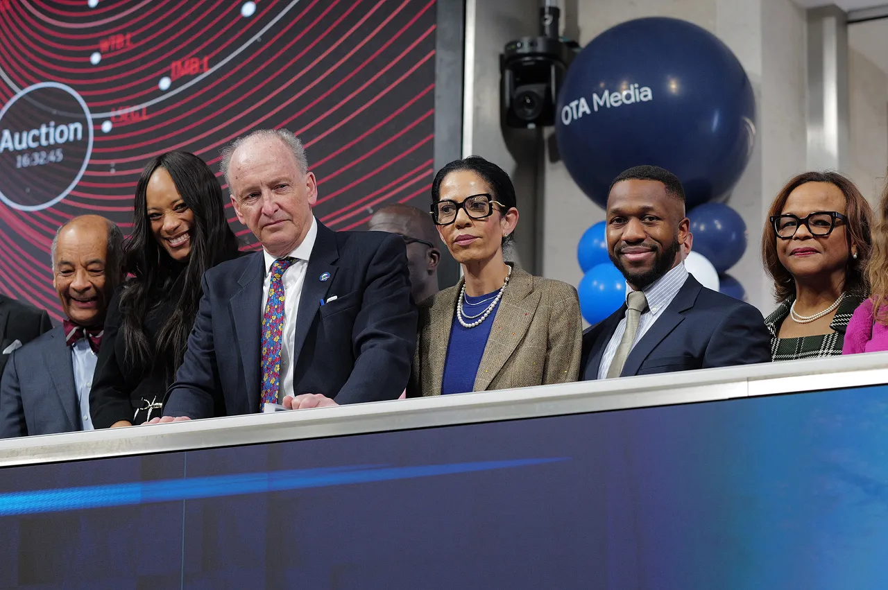 Group of six diverse business professionals standing behind a podium with a digital auction countdown and OTA Media balloons in the background.