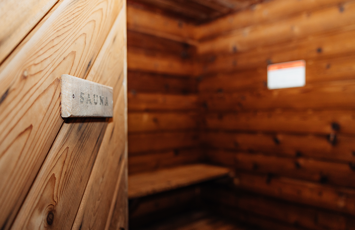 Wooden sauna interior with log walls, a bench, and a wooden door with a SAUNA sign.
