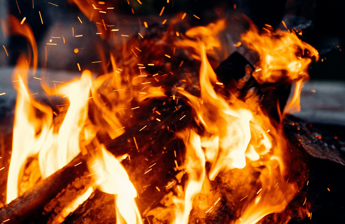 Close-up of bright orange flames and sparks from a burning campfire with logs.