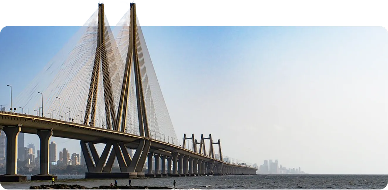 Long cable-stayed bridge over water with city skyline in the background under a clear sky.