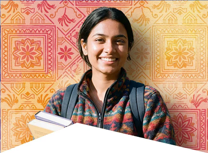 Smiling young woman with backpack holding books against a colorful patterned wall.