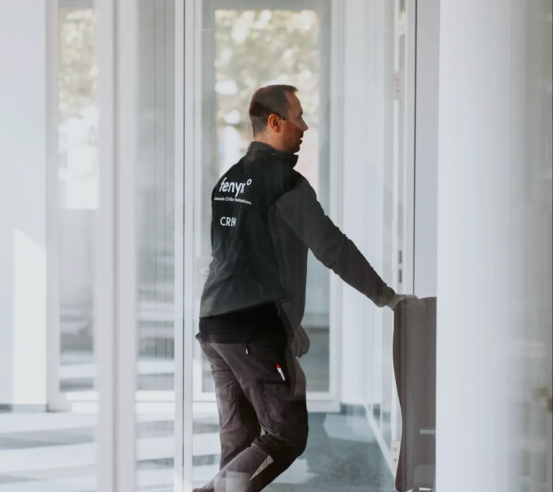 Man in black jacket pushing an office chair through a glass-walled corridor.