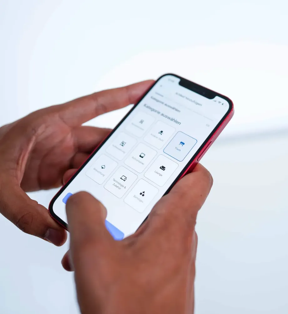 Person holding a smartphone displaying a furniture selection app with categories like tables, lounge, and technology accessories.