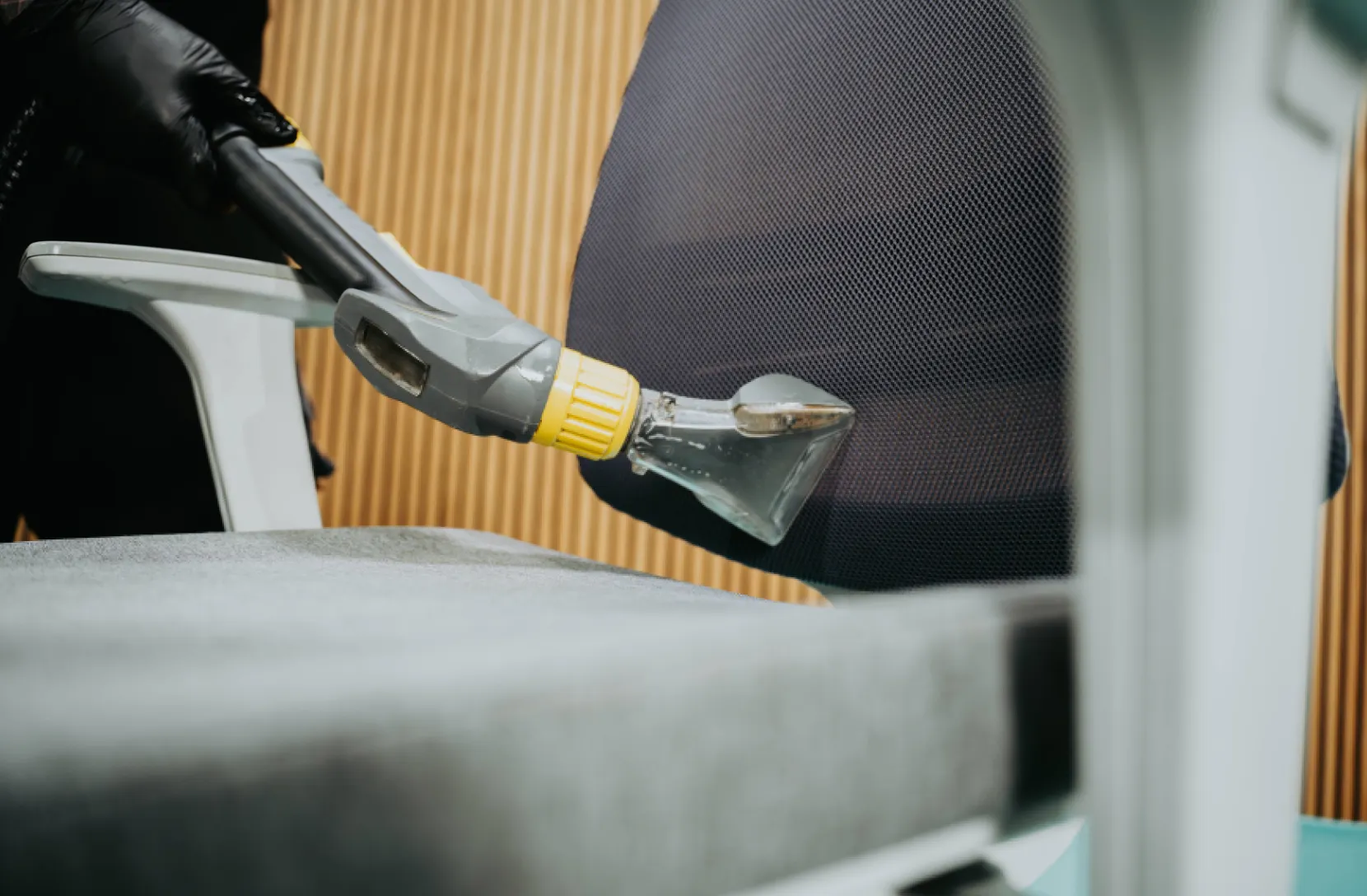 Close-up of a person using a handheld upholstery cleaning tool on a chair seat and backrest.