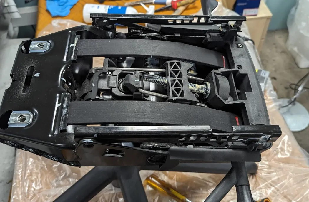 Close-up of a black office chair mechanism showing the tilt and tension control system with springs and metal levers.