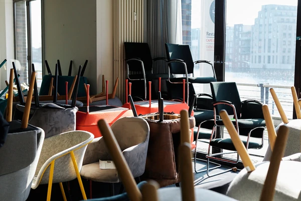 Stacked chairs with their legs pointing up in a sunlit room with large windows.