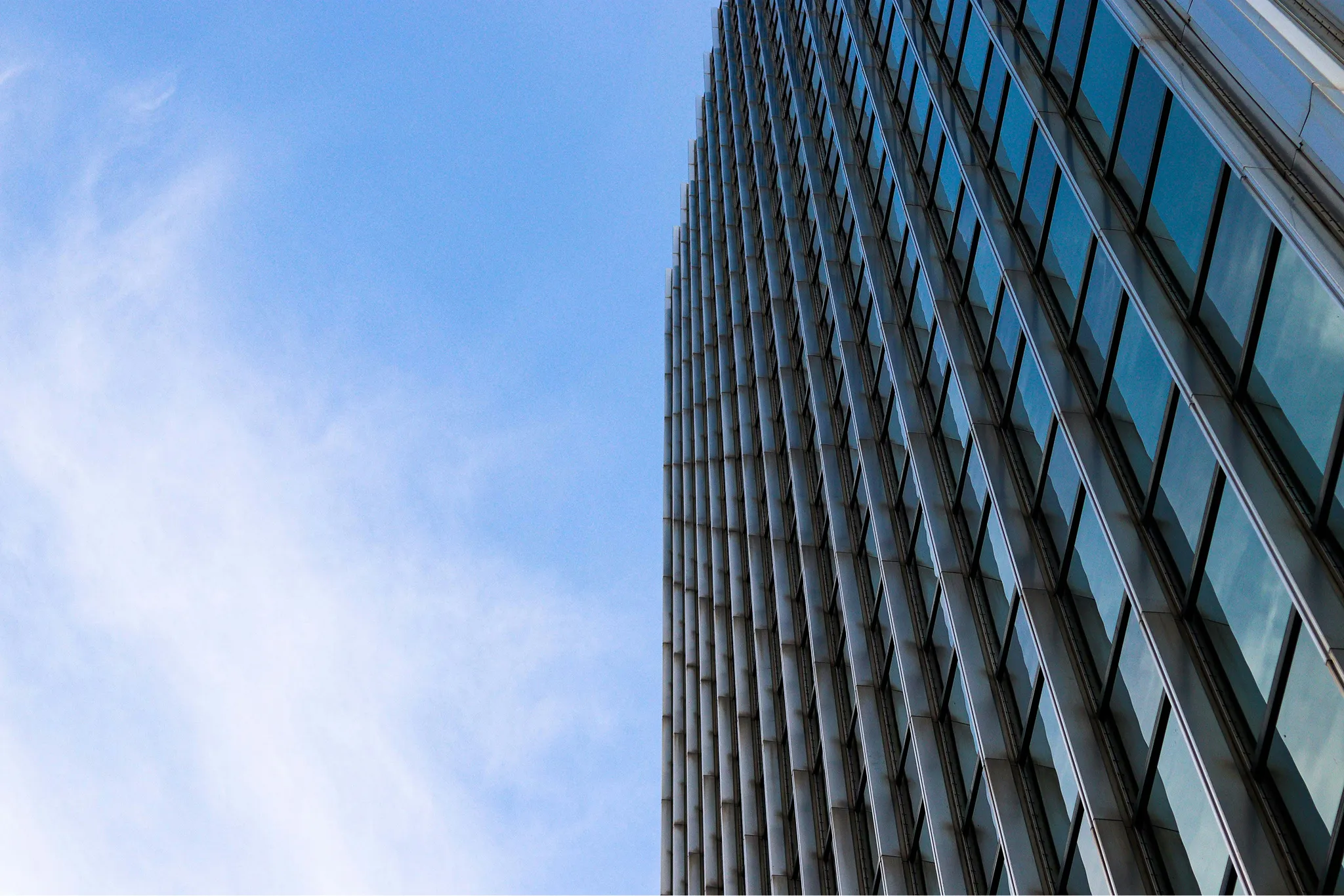 Tall modern glass building reflecting clouds under a clear blue sky.