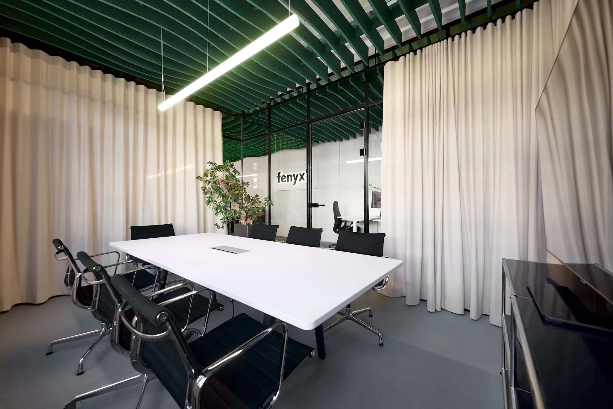 Modern conference room with white table, black chairs, green ceiling panels, and glass walls with the word 'fenyx'.