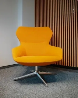 Bright yellow modern swivel chair with metal base on gray carpet in front of wooden slatted wall.