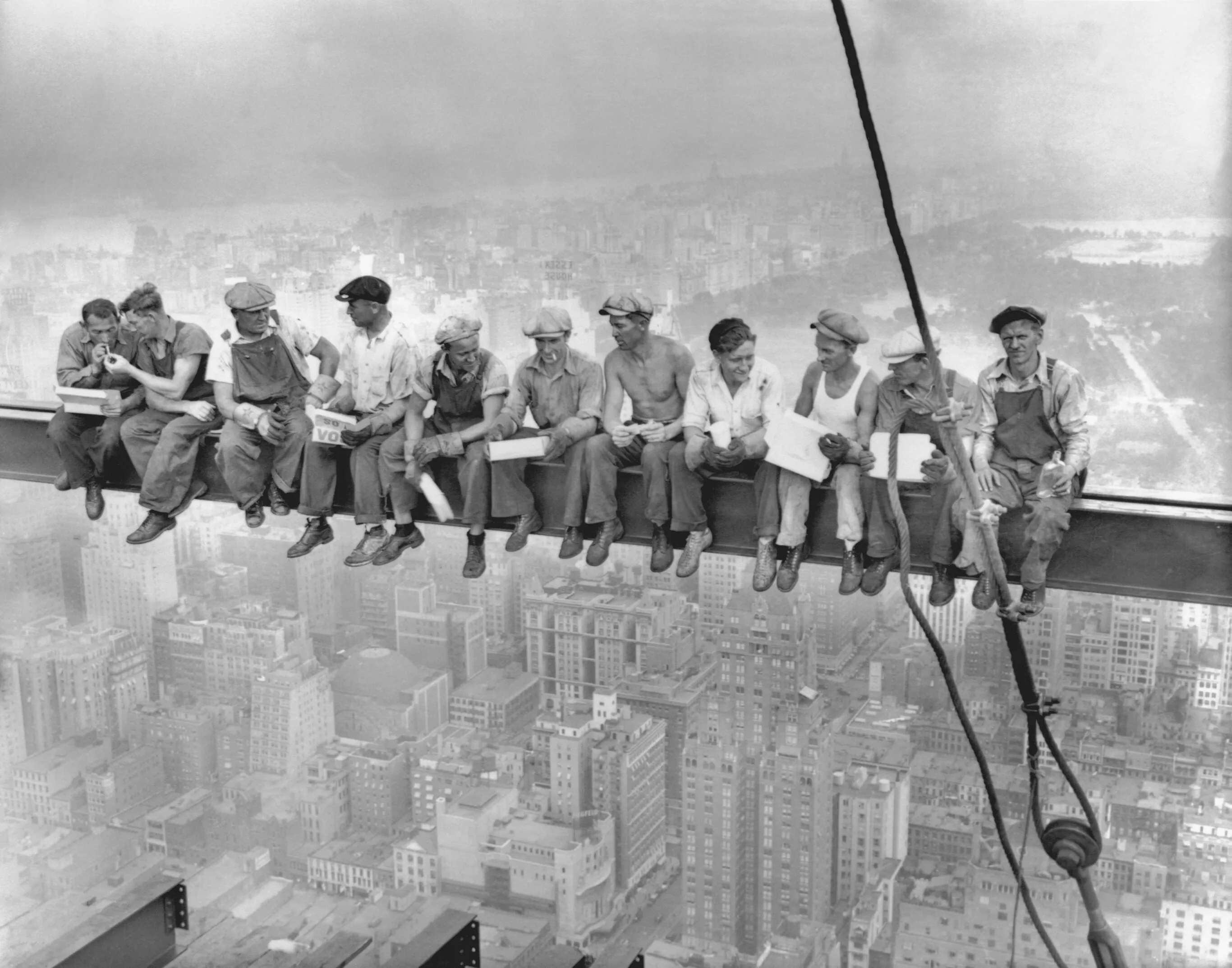 Eleven construction workers sitting on a steel beam high above New York City, eating lunch during skyscraper construction.