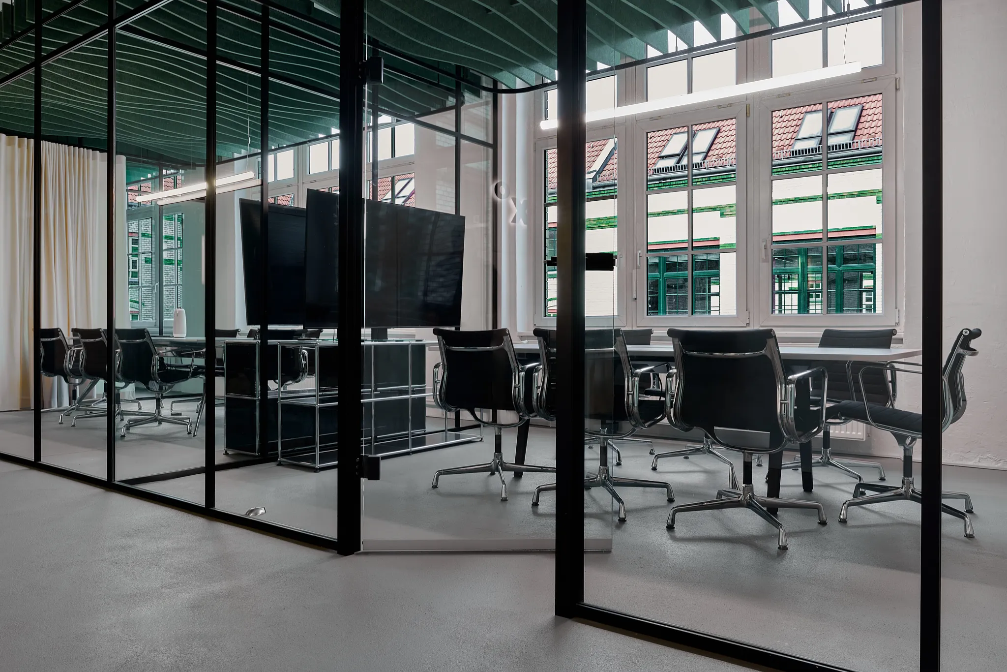Modern glass-walled conference room with black swivel chairs around a white table and large monitors.