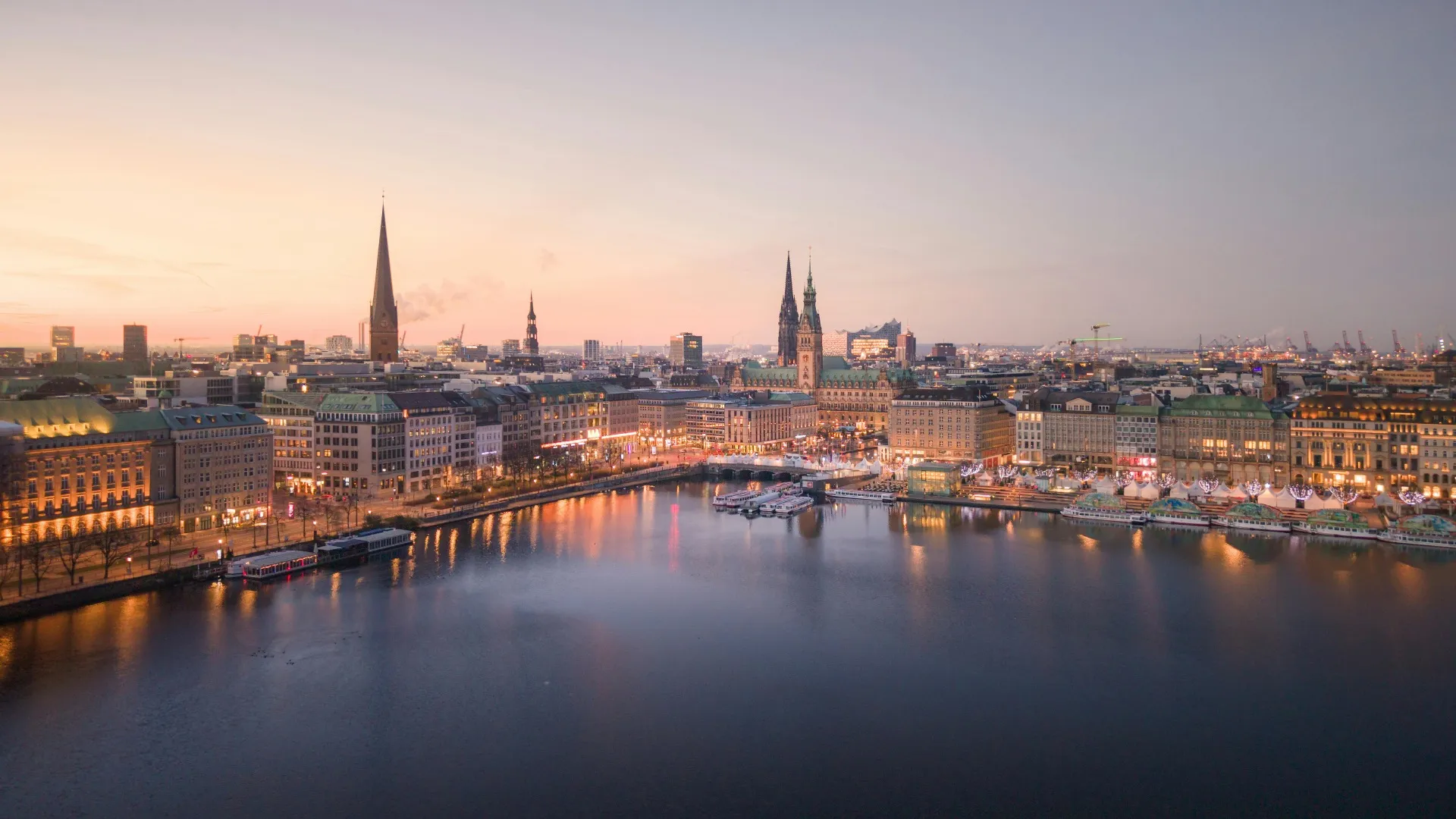 Hamburg cityscape at dusk with illuminated buildings and water reflecting the lights.