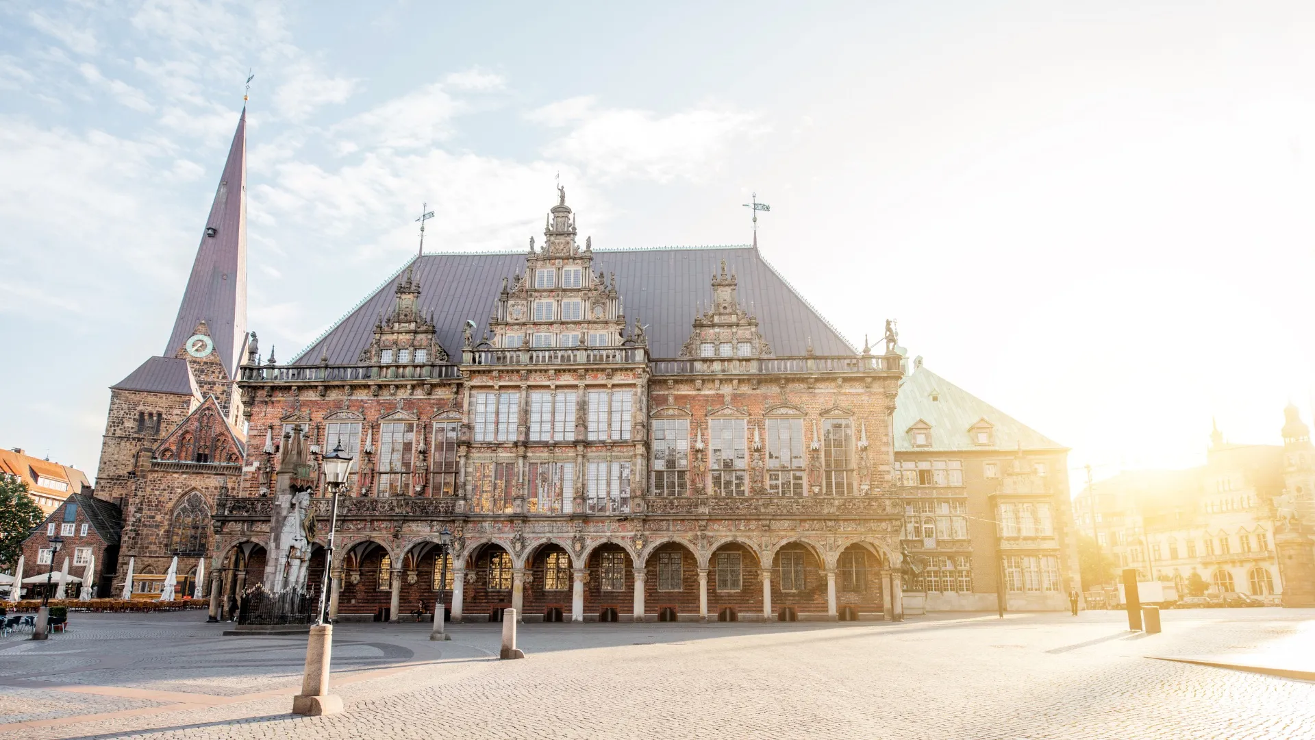 Historisches Rathaus in Bremen mit steinerner Fassade und spitzem Kirchturm im Hintergrund bei Sonnenlicht.
