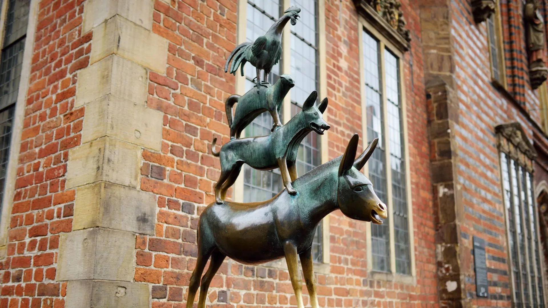 Bronzeskulptur der Bremer Stadtmusikanten mit Esel, Hund, Katze und Hahn vor Backsteinwand.
