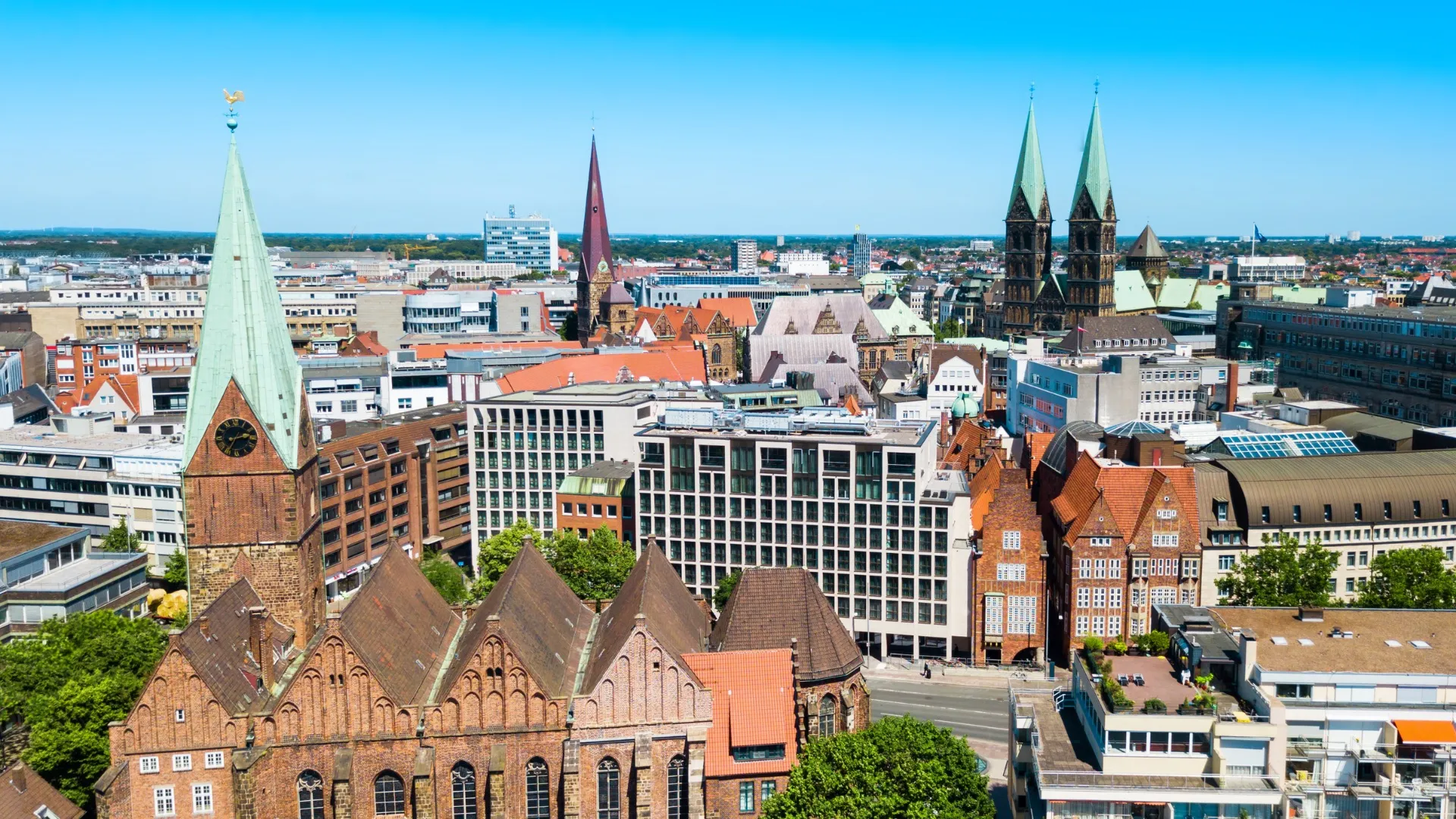 Luftaufnahme der Stadt Bremen mit historischen Kirchtürmen und modernen Gebäuden bei klarem Himmel.