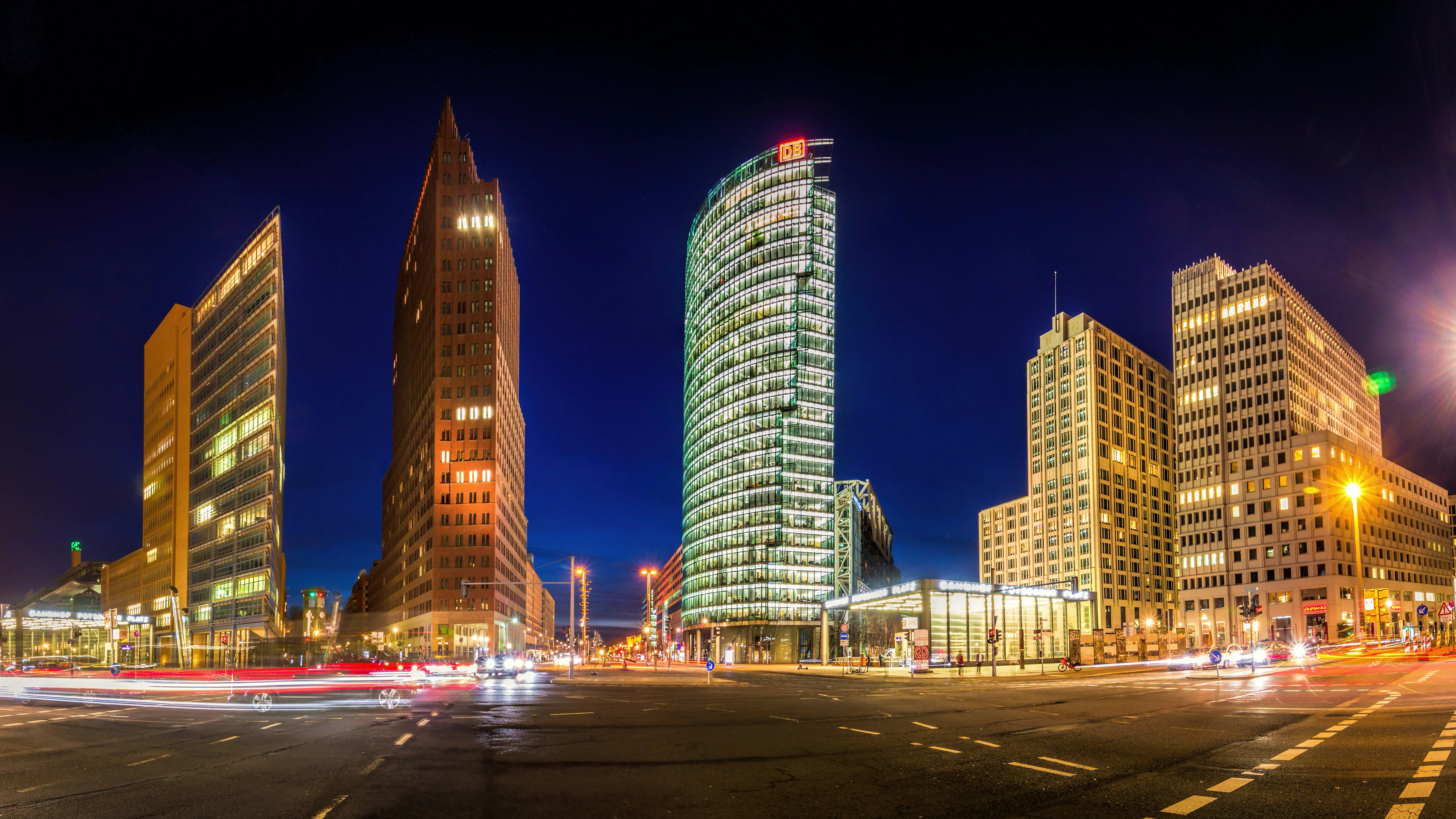 Potsdamer Platz in Berlin bei Nacht mit dem DB-Tower und dem Kollhoff-Tower vor tiefblauem Abendhimmel, belebte Kreuzung mit Lichtstreifen des Verkehrs.