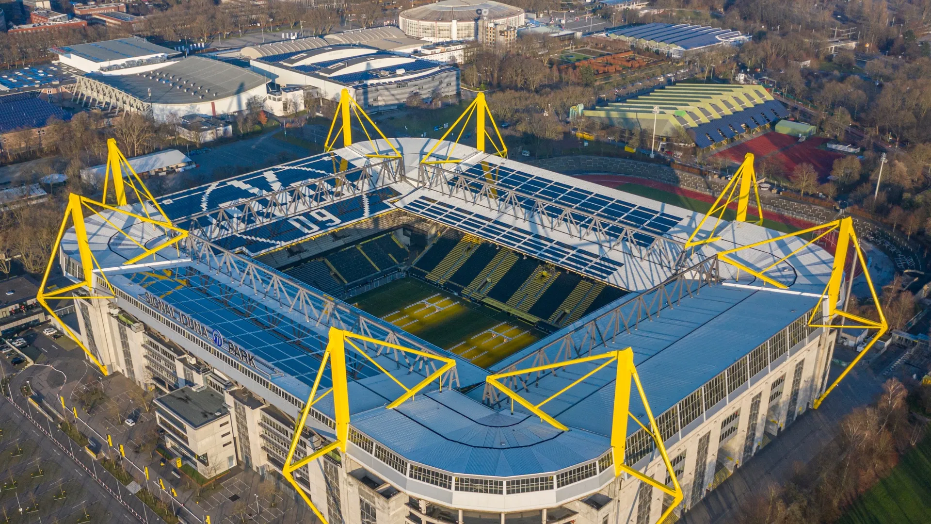 Luftaufnahme des Signal Iduna Parks, eines großen Fußballstadions mit gelben Stahlträgern in Dortmund.
