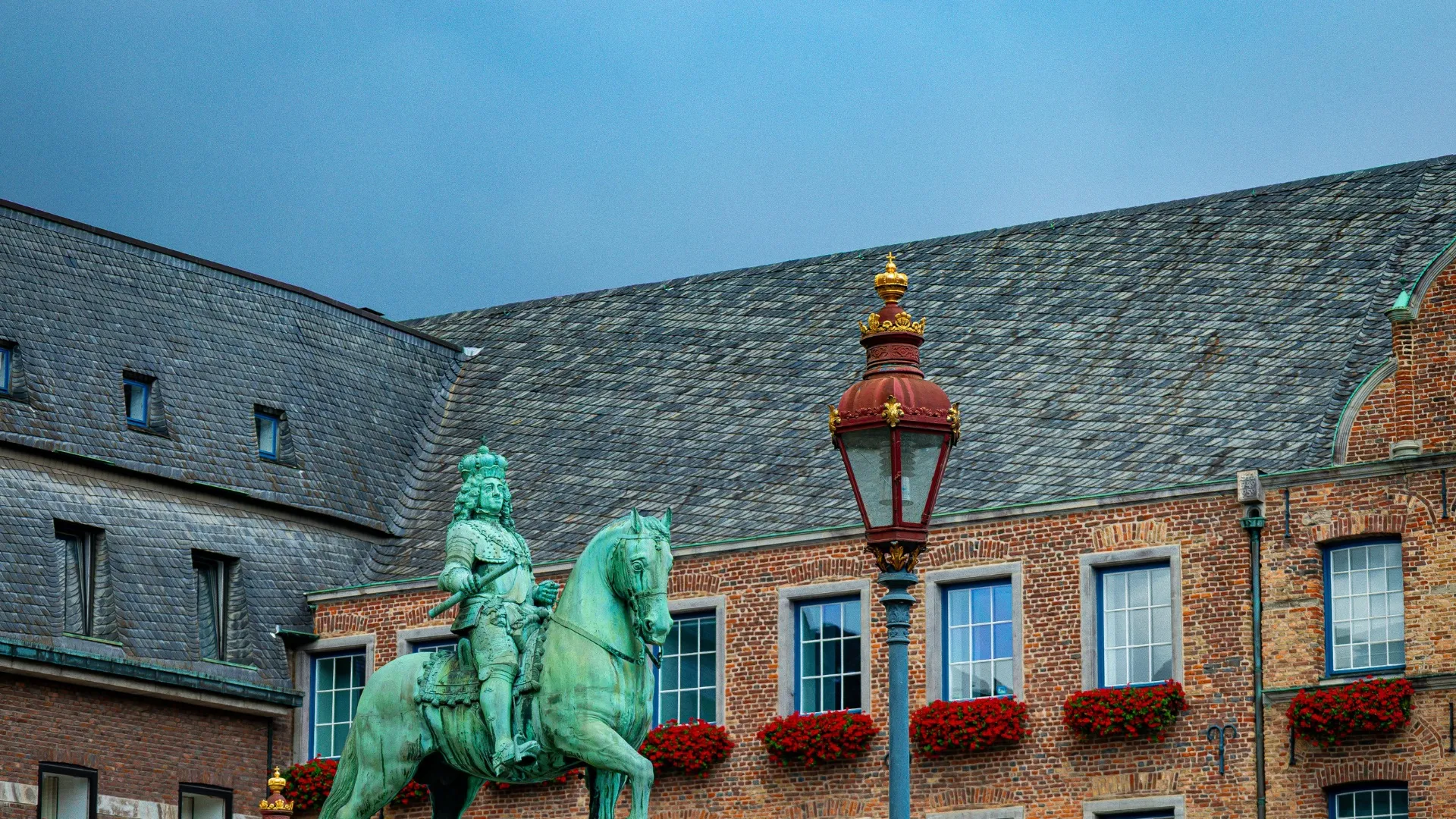 Reiterstatue vor historischem Backsteingebäude mit roten Blumen und Laterne in Düsseldorf.