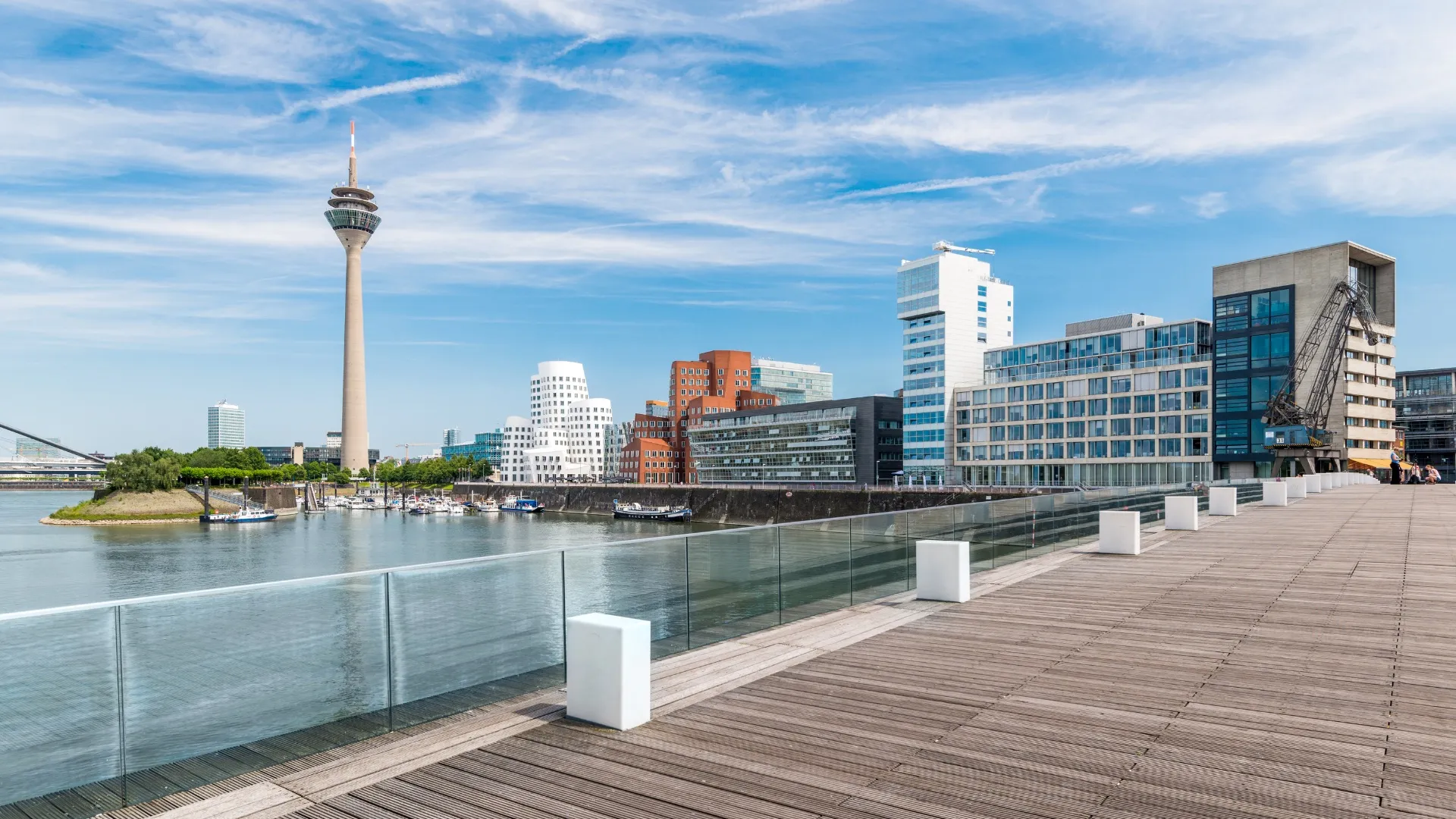 Blick auf Düsseldorfs Medienhafen mit Rheinturm, moderner Architektur und Booten am Wasser.