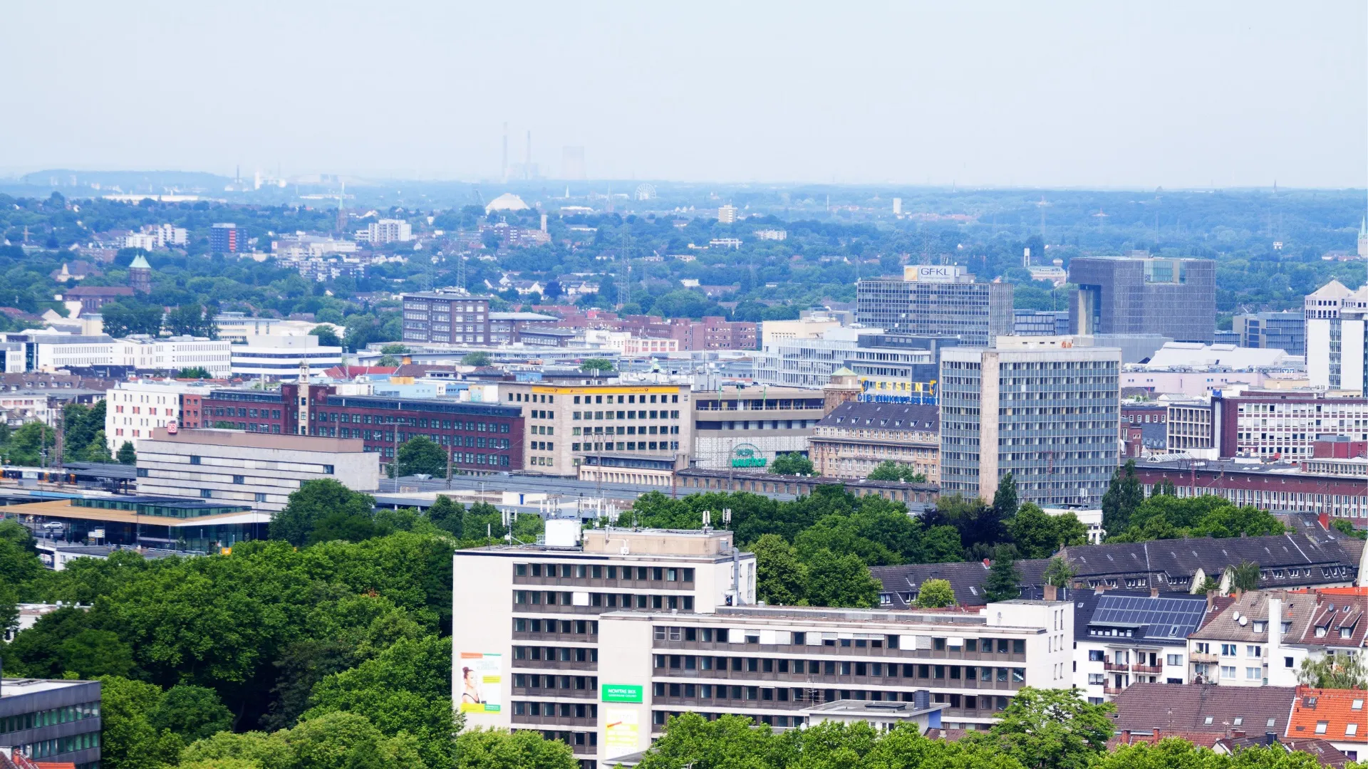 Luftaufnahme der Stadt mit Gebäuden, Bäumen und bewölktem Himmel im Hintergrund.