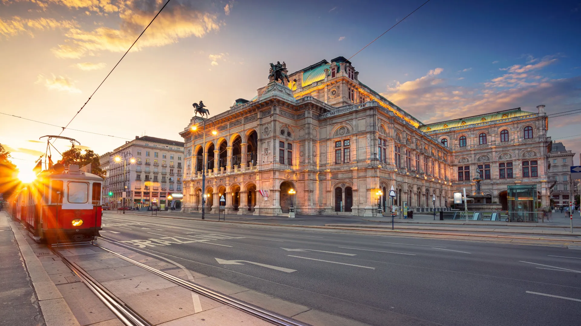Rotes Straßenbahn fährt am Abend an der beleuchteten Wiener Staatsoper vorbei.