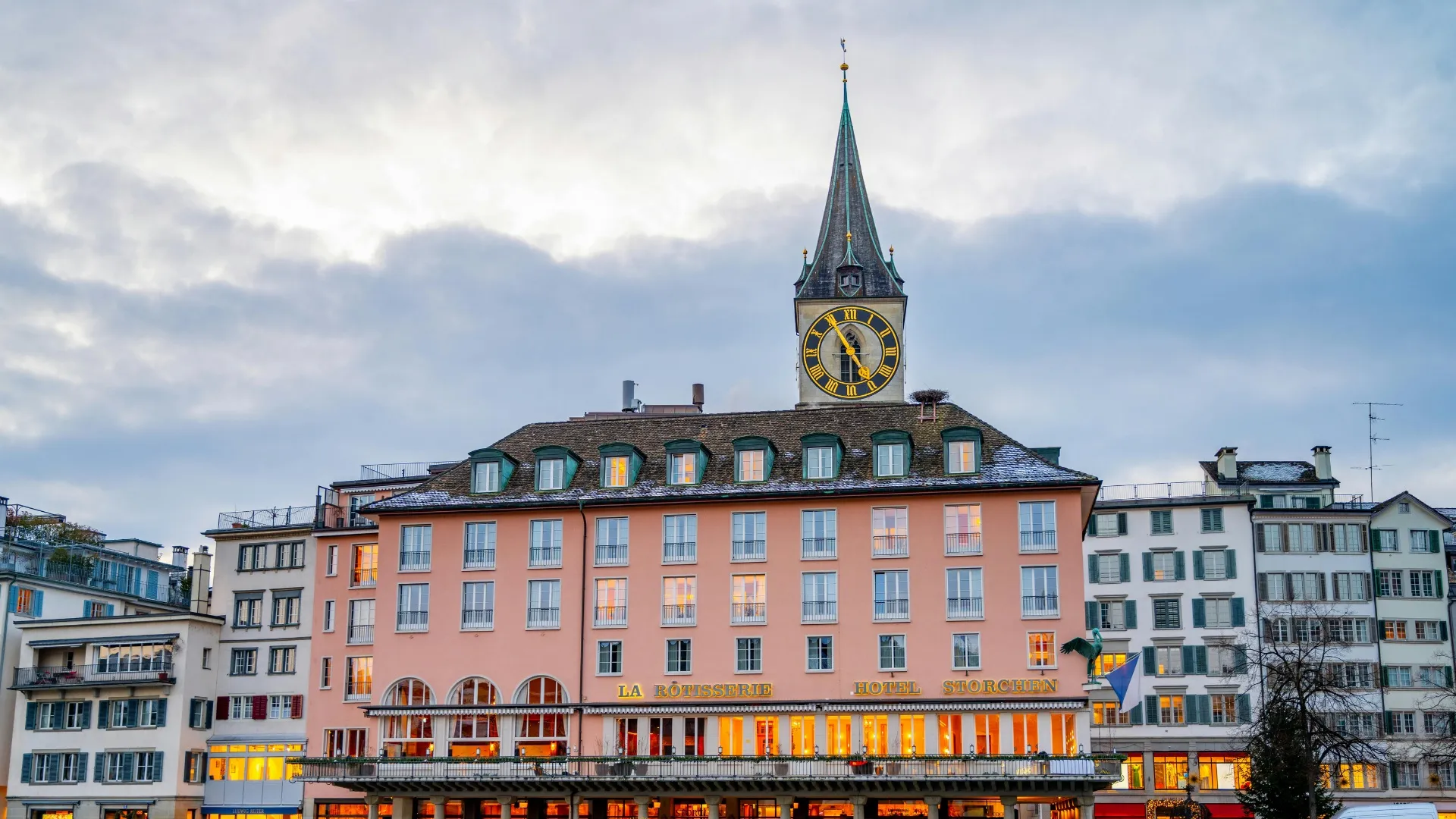 Hotel Storchen mit Uhrturm und beleuchteten Fenstern bei bewölktem Himmel in Zürich.