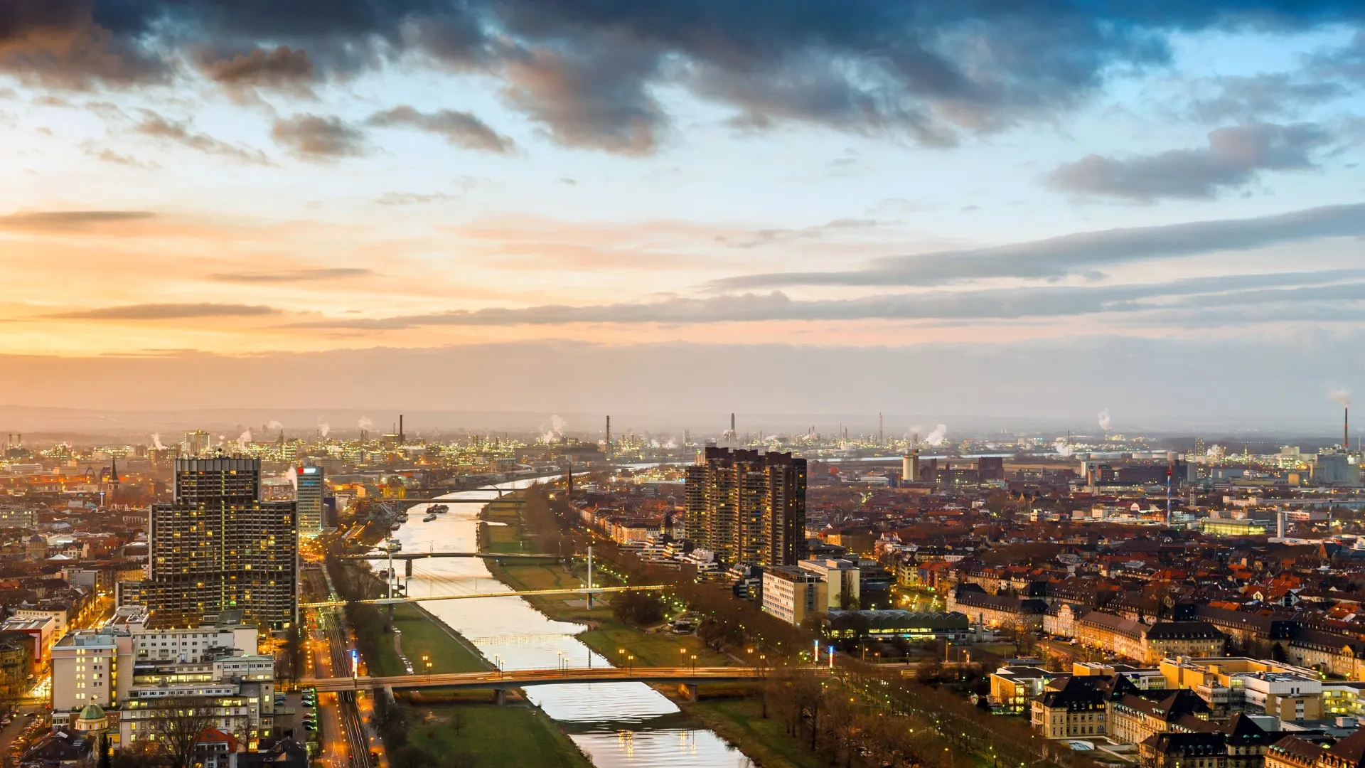 Blick auf Mannheims Stadtzentrum mit Rhein und Hochhäusern bei Sonnenuntergang.