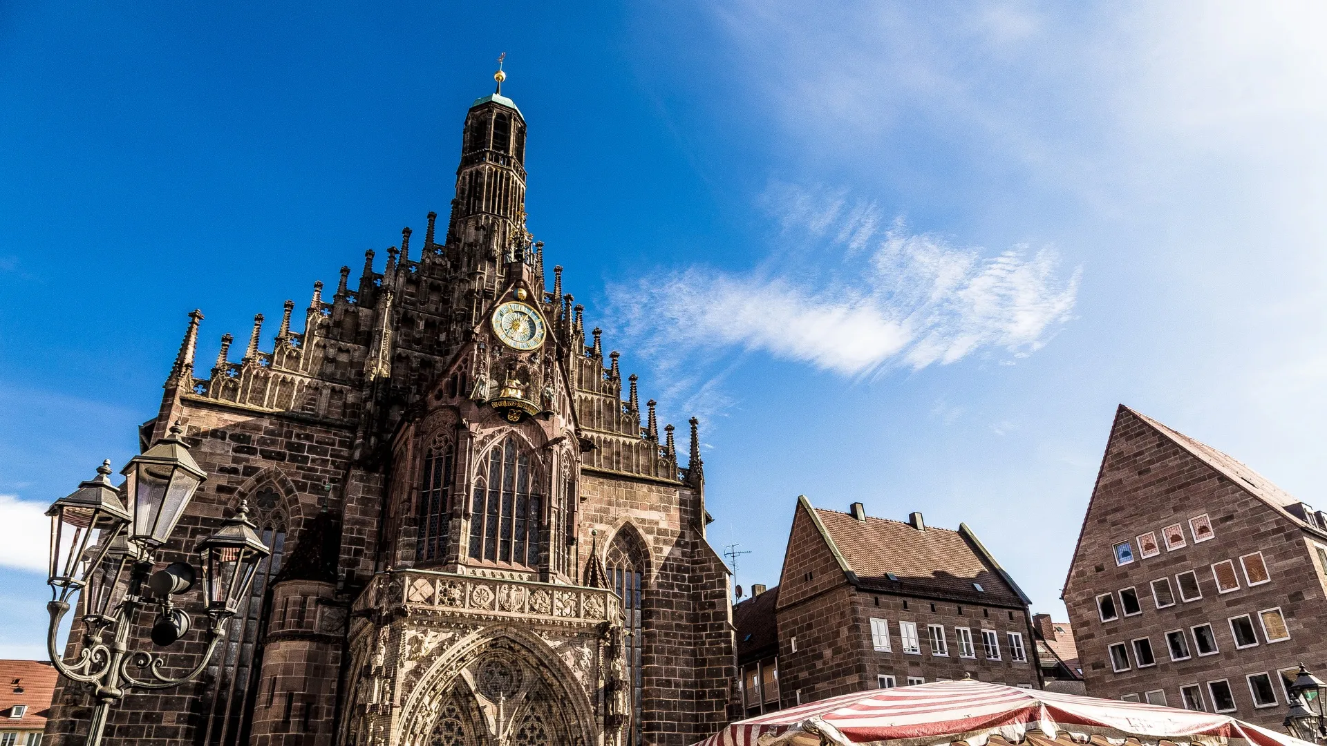 Gotische Kirche mit großer Uhr und Spitze unter blauem Himmel neben traditionellen Häusern.