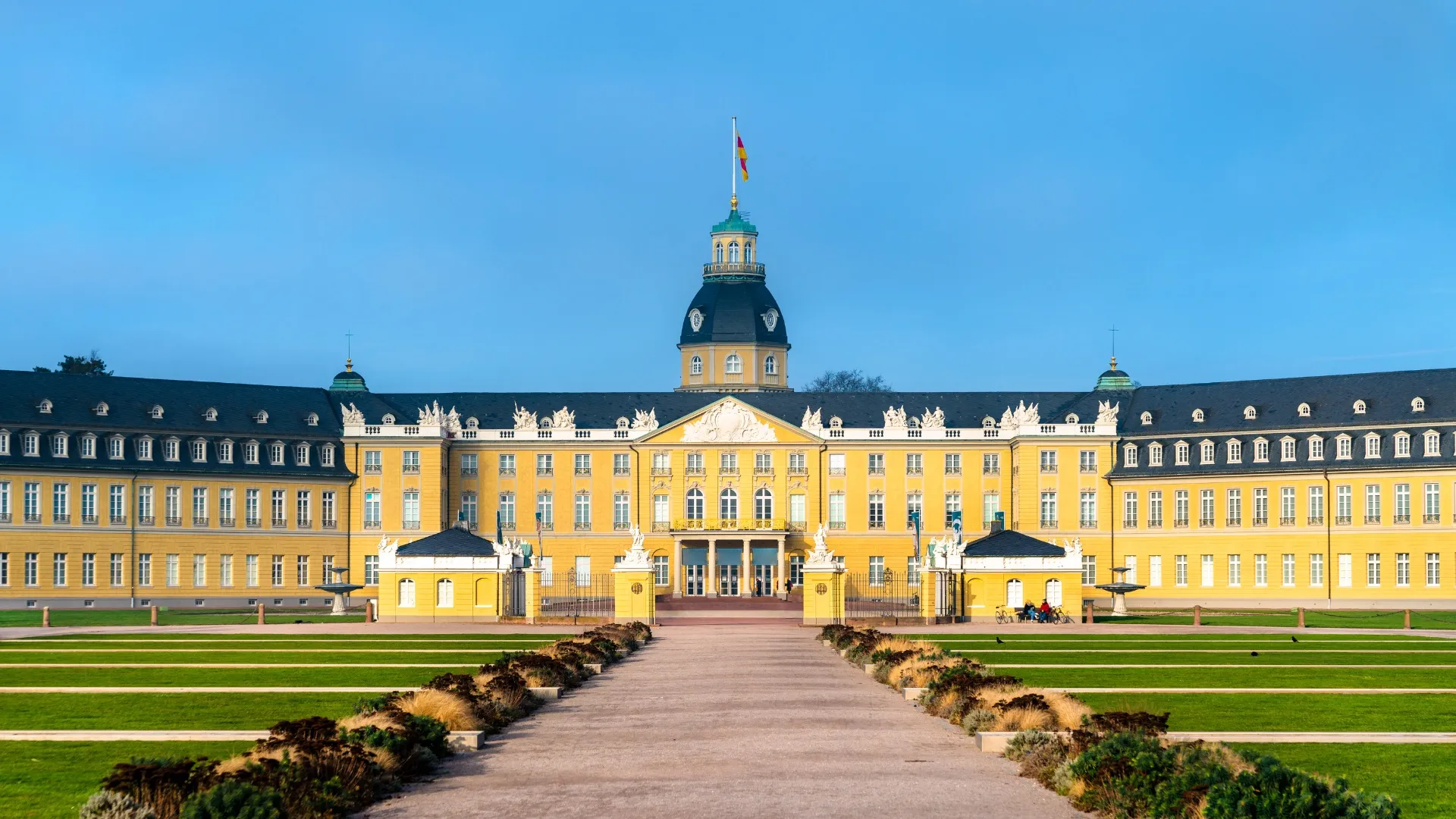 Blick auf das prächtige Schloss Karlsruhe mit gelber Fassade und blauem Himmel im Hintergrund.