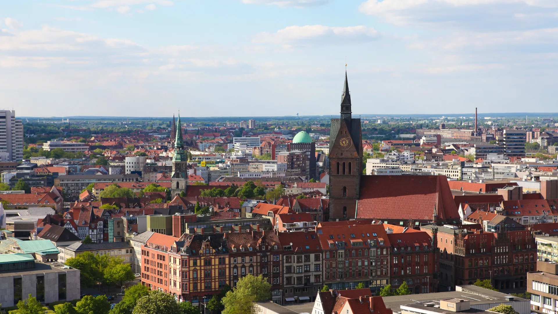Panoramablick auf Hannovers Stadt mit markanten Kirchtürmen und roten Ziegeldächern bei sonnigem Himmel.