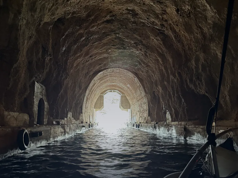 Boat entering a historic submarine tunnel with light at the end in Boka Bay Montenegro