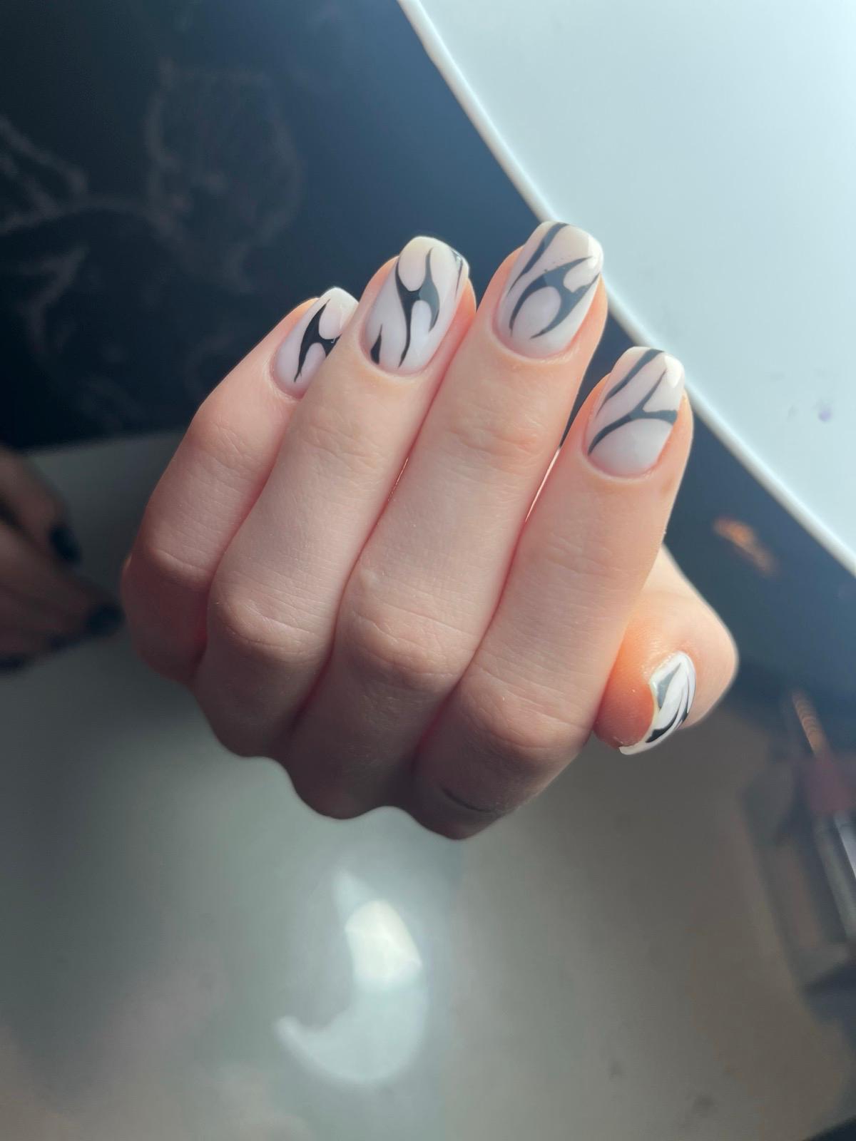 Hand with nails painted in light beige and decorated with abstract black flame-like designs.