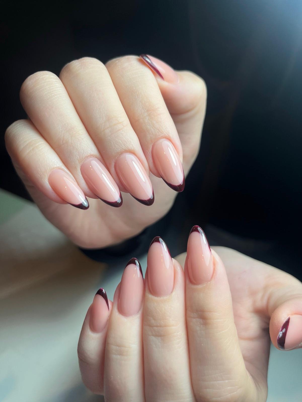 Handen met ovale, nude gekleurde nagels met donkere, puntige Franse manicure tips.